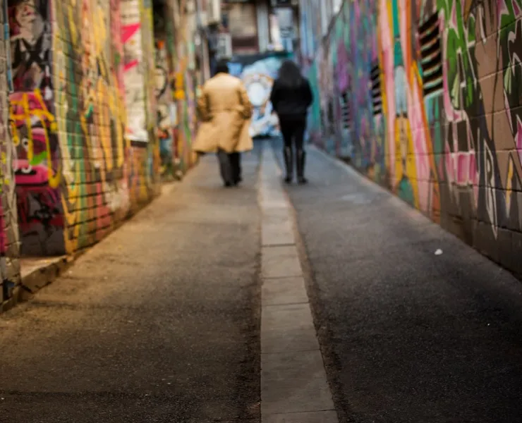 Two people walk side by side, facing away from the camera, down a graffiti-covered alleyway in Melbourne.
